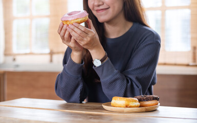 Closeup image of a young woman holding and enjoyed eating donuts at home