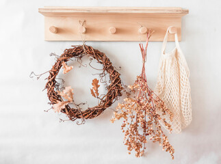 Autumn mood still life - wooden shelf with a vine wreath, dried flowers, fabric bag in a bright room. Cozy eco home style