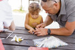 child girl makes paper crafts with dad in the park at a table on a summer day