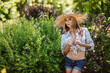 Sexy portrait of a beautiful young woman in a straw hat short shorts and an unbuttoned shirt with a bare thin stomach in a summer park