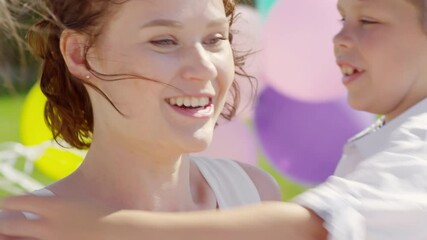 tilt up shot of happy beautiful mother in party hat hugging and kissing little daughter and son whil