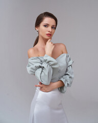 Studio portrait of young beautiful stylish woman with perfect make-up and pony tail brunette hair in green top and silver skirt posing against grey background
