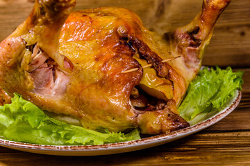 Plate with roasted whole chicken and lettuce leaves on a wooden table