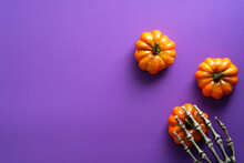 Happy Halloween Holiday Composition With Pumpkins And Skeleton Hand On Violet Background. Flat Lay, Top View, Copy Space.