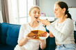 © Iryna - Happy cheerful young woman and her nice looking mother sitting on coach try fruit marshmallow while preparing berry pastille, dish with fresh fruits at home. Healthy food, homemade sweets concept.