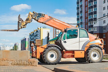 Powerful Wheel Forklift With Telescopic Mast At The Construction Site Of A Modern Residential Area. Construction Equipment For Lifting And Moving Loads.
