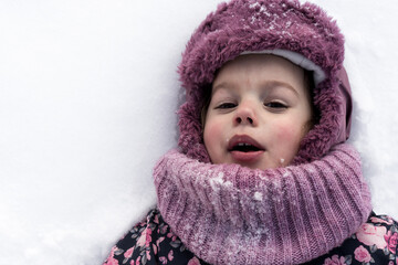 Winter, family, childhood concepts - close-up portrait authentic little preschool girl in pink clothes smile laugh shout with open mouth laying on snow in frosty weather day outdoors. Funny kid face