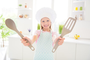 Photo of young cheerful little girl happy positive smile show kitchen cutlery spatula ladle cuisine indoors