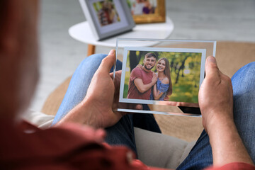 Wall Mural - Senior man holding frame with photo of young couple at home, closeup