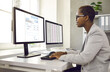 © Studio Romantic - African American female accountant working with software for electronic invoices on computer. Side view of a smiling woman sitting at a table with a laptop and a desktop computer in a modern office.