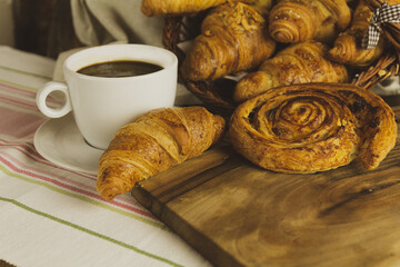 Canvas Print - Closeup shot of croissants, a sweet roll and a cup of coffee on a wooden background