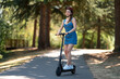 © Anton - A girl in a protective helmet rides in the park on a bicycle path on an electric scooter. Sunny day, beautiful nature. There are no people around. New technologies, environmentally friendly transport.