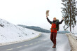 Young caucasian hitchhiker resenting about failed attempt to stop the car on a winter mountain road. Backpacker hitchhiking with a cardboard sign, copy space. Traveling and hitchhiking concept 