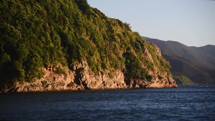 Sticker - A beautiful view of the hill covered in trees near the water on a sunny day in HD