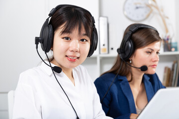 Wall Mural - Friendly smiling Chinese woman helpline operator with headset using computer at office