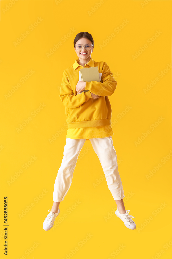 Jumping young woman with books on color background