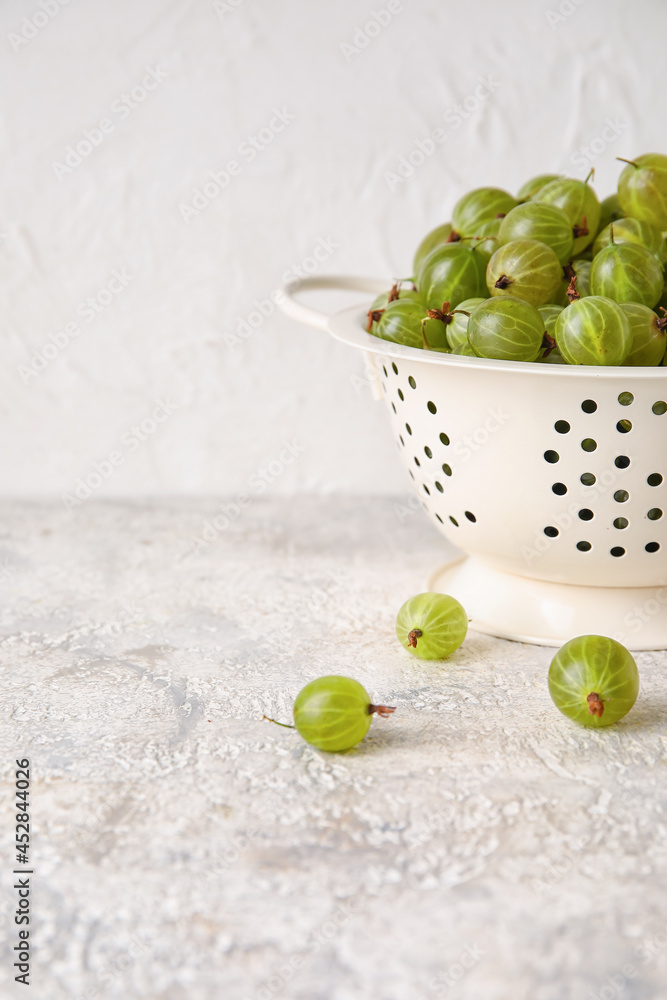 Colander with fresh ripe gooseberry on table