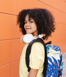 © PintoArt - handsome boy with afro hair, going to preschool, with backpack and headphones, vertical photo