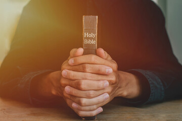 Hands of a man praying over a Bible represents faith and spirituality in everyday life. close up.