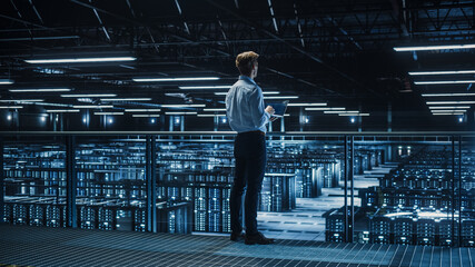 Leinwandbilder - Handsome Smiling IT Specialist Using Tablet Computer in Data Center. Succesful Businessman and e-Business Entrepreneur Overlooking Big Server Farm for Cloud Computing.