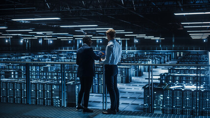Poster - Data Center Male IT Specialist and Female e-Business Enrepreneur Talk, Use Laptop. Two Information Technology Professionals on Bridge Overlooking Big Cloud Computing Server Farm.