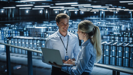 Wall Mural - Data Center Female e-Business Enrepreneur and Male IT Specialist talk, Use Laptop. Two Information Technology Professionals on Bridge Overlooking Big Cloud Computing Server Farm.