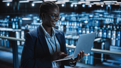 Data Center Female Programmer Using Laptop Computer, Maintenance IT Specialist. In Cloud Computing Server Farm Smiling System Administrator Working on Cyber Security for Iaas, saas, paas.