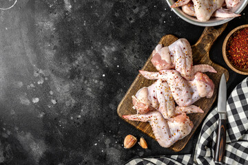 Wall Mural - Raw chicken wings on a wooden board on a dark culinary background top view from a copyspace. The process of cooking poultry