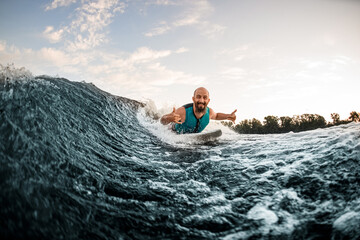 Wall Mural - athletic male wakesurfer lying on the board rides down the river wave