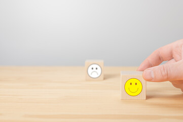 man points his finger at a wooden cube with positive face. cube with sign of negative face icon is blurred in gray background. Customer service evaluation and satisfaction survey service rating