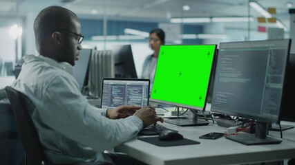 Wall Mural - Multi-Ethnic Office: Black IT Programmer Working on Computer with Green Screen Chroma Key Display. Male Software Engineer Developing App, Program, Video Game. Terminal with Code Language. Static Shot