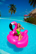 Beautiful sexy tanned woman bikini model on pink flamingo in pool. Young glamour girl in swimsuit on Maldives island. Perfect body bikini model in luxury resort on Maldives. Luxury travel, lifestyle.