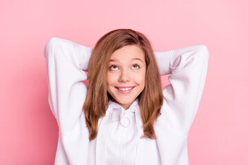 Poster - Photo of shiny charming school girl wear white hoodie smiling arms behind head looking up empty space isolated pink color background