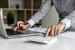© kamiphotos - Businesswoman using a white calculator, a financial businessman examining the numerical data on a company financial document, she uses a calculator to verify the accuracy of numbers.