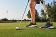Professional golfer with prosthetic leg hitting with putter on golf ball during golfing. Concept of willpower of people with disabilities in sport