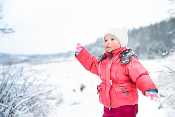 Funny girl in winter pink jumpsuit on background of snow-capped hills and bushes in snow. Child outdoors in frosty weather. benefits of walking for children