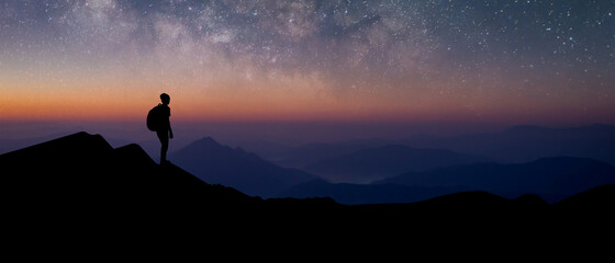 Panorama silhouette of young traveler with backpack standing and watched the star and milky way alone on top of the mountain. He enjoyed traveling and was successful when he reached the summit.