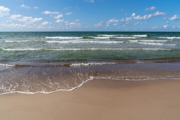 Sticker - idyllic sandy beach with gentle waves lapping at the shore under a blue summer sky with white clouds and coyp space