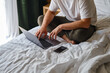 © Iuliia Pilipeichenko - A man works with a laptop and smartphone in bed at home or in hotels. Remote work. Office at home. A man in the bedroom is typing on a laptop, distance learning for students, surfing the Internet