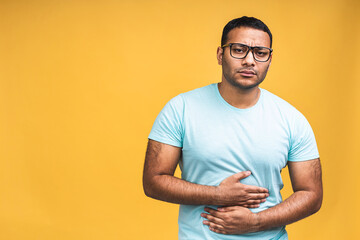 Young handsome african american black indian man with hand on stomach because indigestion, painful illness feeling unwell isolated over yellow background. Abdominal pain concept.