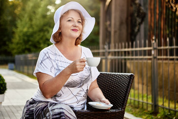 Wall Mural - Elderly woman sits in park and drinks coffee at daytime.