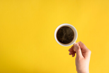 Flat lay of female woman hand holding cup of espresso coffee with copy space on yellow background