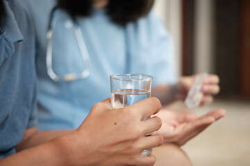 Wall Mural - Close-up photo of female doctor's hand holding a glass of water while helping a male elderly patient take medicine It is a home medical service for retired elderly people.