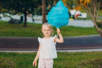 Wall Mural - Little blond girl eating blue cotton candy in the park