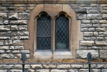 Detailed View Of A Very Old European Stone Church Wall And Leaded Windows Seen Behind Part Of A Wrought Iron Fence.