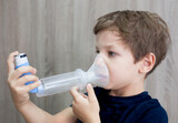 Fototapeta  - Child boy using medical spray for breath. Inhaler, spacer and mask. Side view