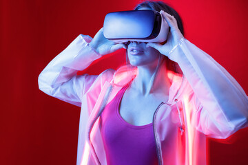 Woman in futuristic costume. Girl in glasses of virtual reality. Augmented reality game, future technology, AI concept. VR. Neon red light.