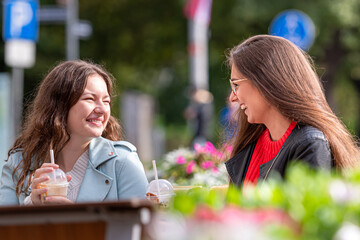 two milenial girlfriend spend free time in outdoor cafe with cocktails, laughing and talking