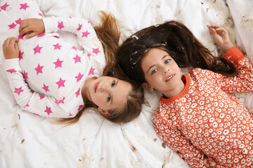 Canvas Print - Cute little girls in pajamas lying among feathers on bed, top view. Happy childhood