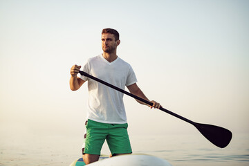 Wall Mural - Young man in t-shirt and shorts floating on SUP board